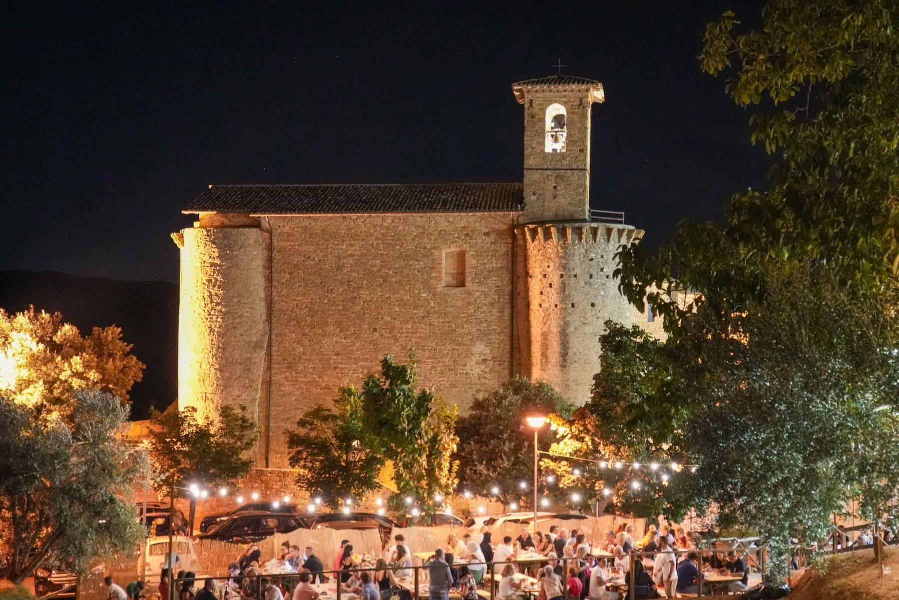 Chiesa illuminata di notte sopra le tavolate della sagra