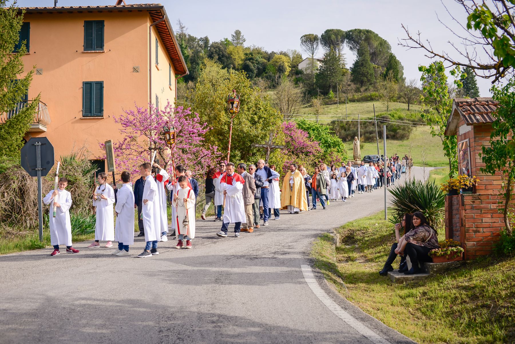 Corteo della processione tra le case del borgo in fiore a primavera